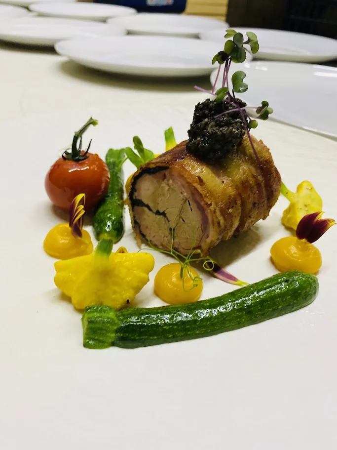 Glazed roasted meat with vegetable purees and edible flowers on a white plate