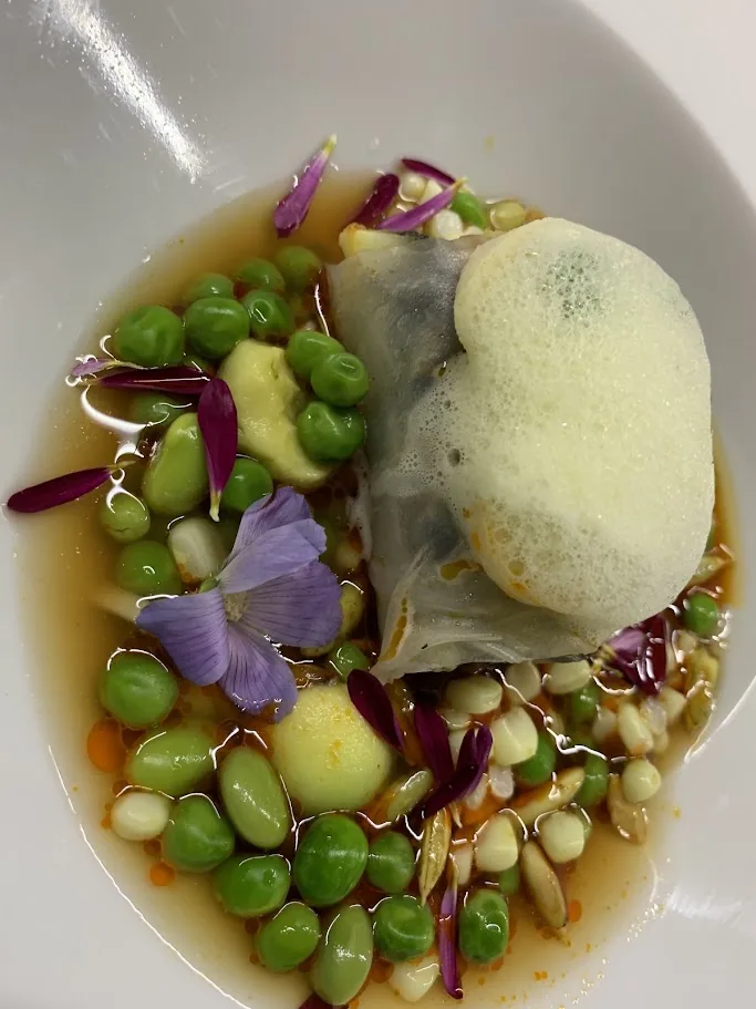 Seasonal plated dish decorated with peas, edible flowers and delicate foam
